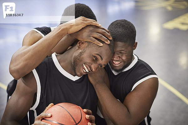Fröhliche junge Basketballspieler umarmen und feiern nach dem Sieg
