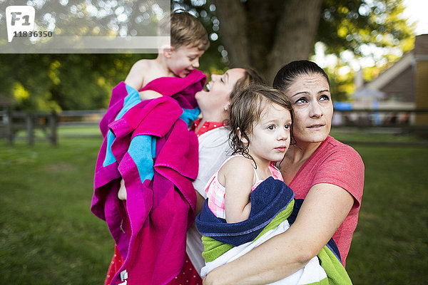 Lesbische Mütter halten nasse Kinder in einem Handtuch im Sommerhof.