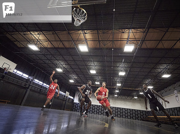 Junge männliche Basketballspieler spielen Basketball auf dem Platz in der Turnhalle.