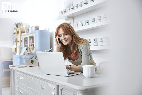 Lächelnde Geschäftsfrau mit Laptop und Handy an der Theke in der Kunstlackiererei