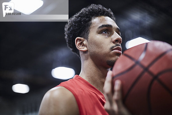 Porträt ernster  fokussierter junger Basketballspieler  der Basketball hält.