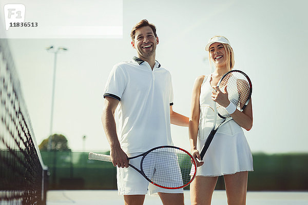 Portrait lächelnde  selbstbewusste Tennisspieler mit Tennisschlägern auf sonnigem Tennisplatz