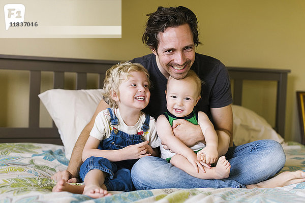 Vater mit Söhnen (12-17 Monate  4-5) auf dem Bett sitzend