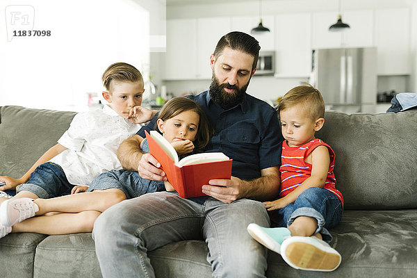 Vater mit seinen drei Kindern (2-3  6-7) beim Lesen eines Buches