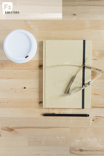 Einwegbecher  Tagebuch  Brille und Stift auf einem Holztisch