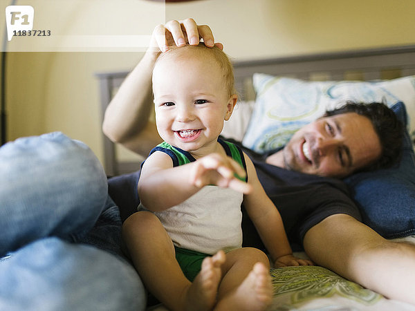 Vater streichelt kleinen Jungen (12-17 Monate) im Schlafzimmer