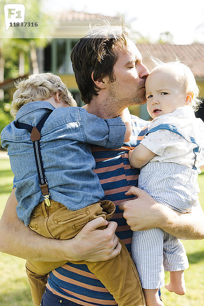 Vater mit zwei Söhnen (12-17 Monate  4-5) beim Spielen im Hinterhof