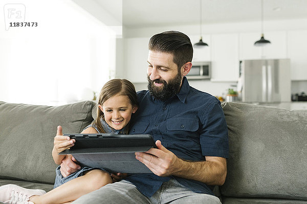 Vater mit Tochter (6-7) bei der Nutzung eines digitalen Tablets im Wohnzimmer