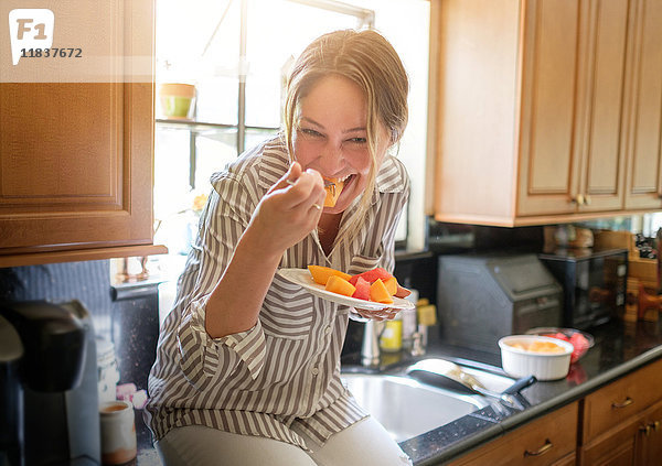 Frau in Küche isst Obstsalat