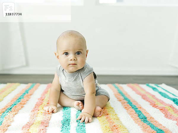 Porträt eines kleinen Jungen (6-11 Monate) auf einem bunten Teppich sitzend