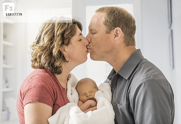 Eltern halten ihren kleinen Sohn (0-1 Monate) und küssen sich