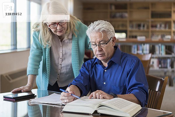 Ältere Frau hilft Mann beim Lesen eines Buches in der Bibliothek