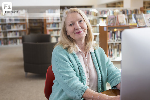 Lächelnde kaukasische Frau am Computer in einer Bibliothek