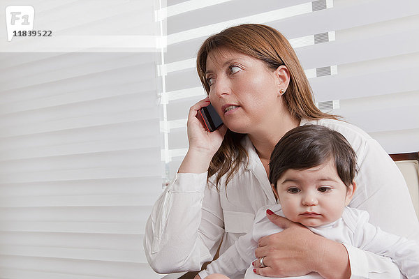 Hispanische Mutter hält ihren kleinen Jungen und spricht mit dem Handy