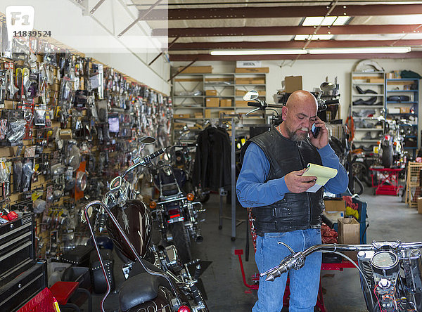 Kaukasischer Mann hält Notizblock in der Nähe eines Motorrads und spricht mit einem Mobiltelefon