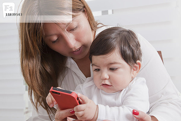 Hispanic Mutter hält Baby Junge spielt mit Handy