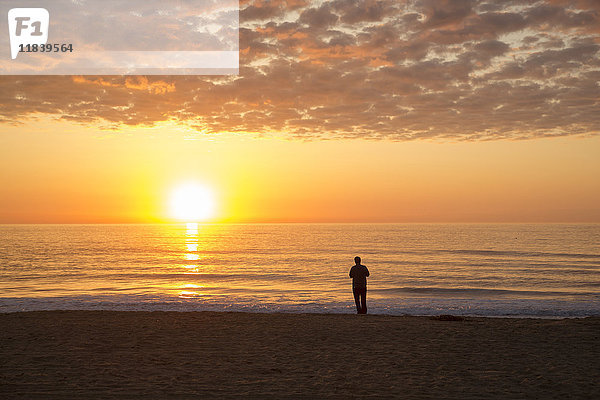 Silhouette eines Mannes  der bei Sonnenuntergang am Strand steht