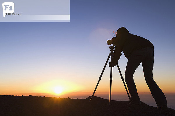 Silhouette eines gemischtrassigen Fotografen mit Kamera bei Sonnenuntergang