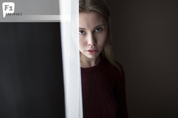 Ernste kaukasische Frau steht in der Nähe eines Vorhangs am Fenster