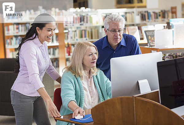 Älterer Mann und Frau benutzen Computer in einer Bibliothek