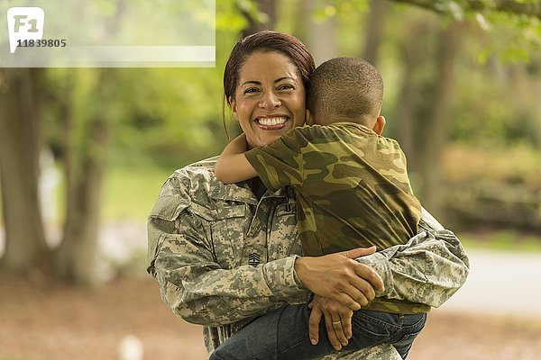 Afroamerikanische Soldatenmutter  die ihren Sohn trägt und umarmt