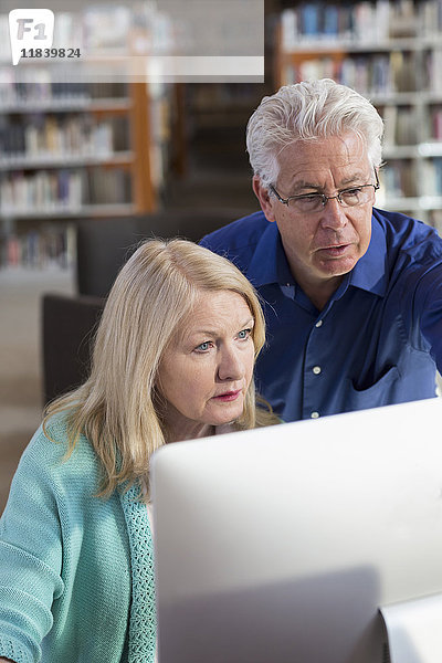 Älterer Mann hilft Frau mit Computer in Bibliothek