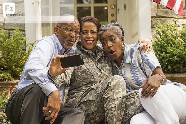 Soldat  der mit seinen Eltern auf der Treppe sitzt und für ein Selfie mit dem Handy posiert