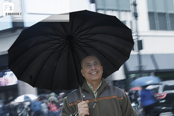 Lächelnder hispanischer Mann mit Regenschirm in der Stadt