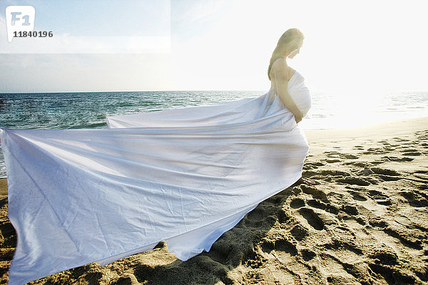 Wind weht Kleid von Mixed Race werdende Mutter am Strand