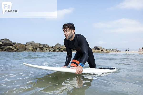 Kaukasischer Mann watet im Meer und hält ein Surfbrett