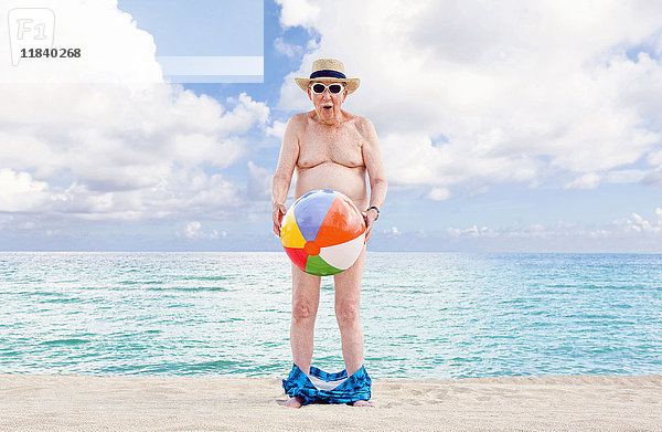 Nackter älterer kaukasischer Mann  der seine Taille mit einem Strandball bedeckt