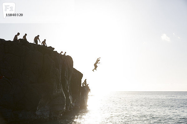 Freunde springen von einer Klippe ins Meer