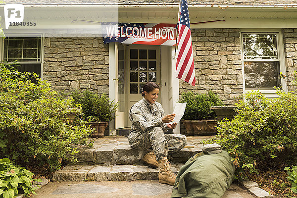 Lächelnder afroamerikanischer Soldat sitzt auf der Treppe und liest einen Brief
