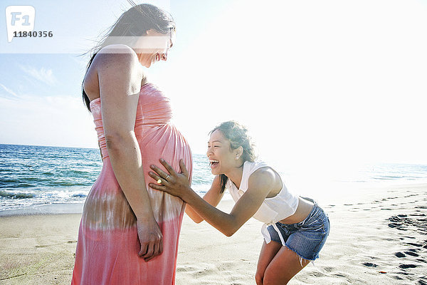 Frau hält Bauch der werdenden Mutter am Strand