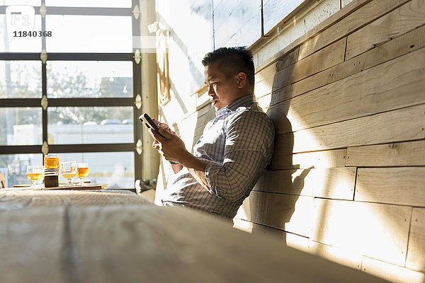 Asiatischer Mann  der in einer Brauereikneipe eine SMS auf seinem Handy schreibt