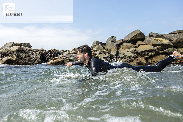 Kaukasischer Mann paddelt auf einem Surfbrett