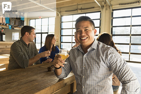 Porträt eines lächelnden Mannes  der mit Freunden in einer Brauereikneipe Bier trinkt