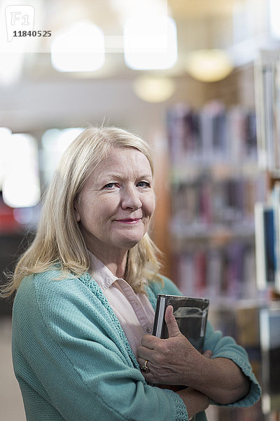 Lächelnde kaukasische Frau mit Buch in der Bibliothek