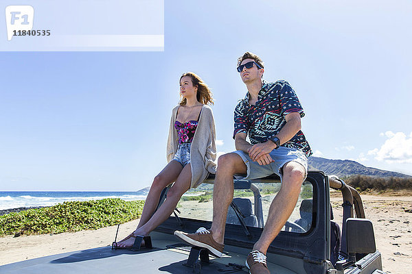 Ehepaar sitzt auf der Windschutzscheibe eines Cabriolets am Strand