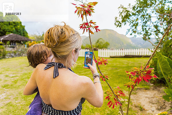 Kaukasische Mutter trägt ihren Sohn und fotografiert ihn mit ihrem Mobiltelefon