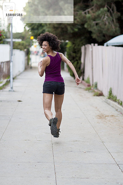 Lächelnde gemischtrassige Frau läuft auf dem Gehweg