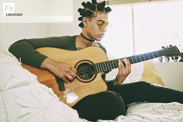 Mixed Race Frau sitzt auf dem Bett und spielt Gitarre