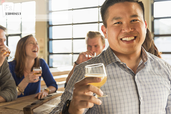 Porträt eines lächelnden Mannes  der mit Freunden in einer Brauereikneipe Bier trinkt