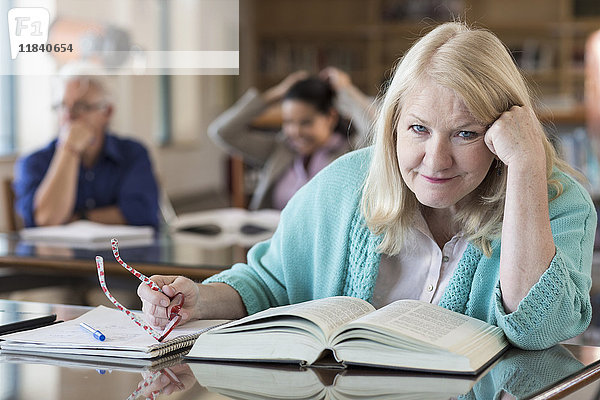 Verwirrte ältere Frau  die in einer Bibliothek ein Buch liest
