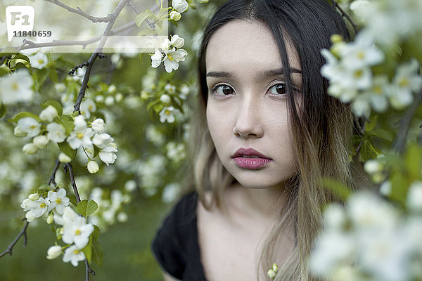 Asiatisches Teenager-Mädchen steht in Zweigen mit Blumen