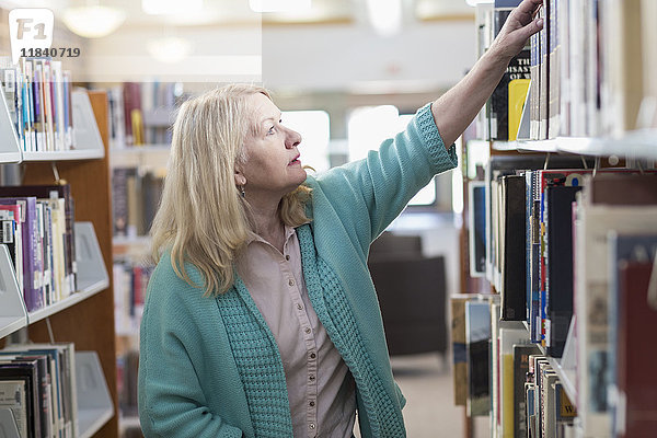 Neugierige kaukasische Frau greift in der Bibliothek nach einem Buch