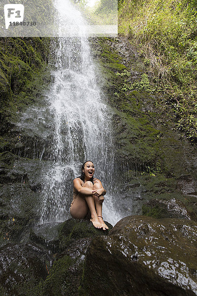 Kaukasische Frau sitzt auf einem Felsen in der Nähe eines Wasserfalls