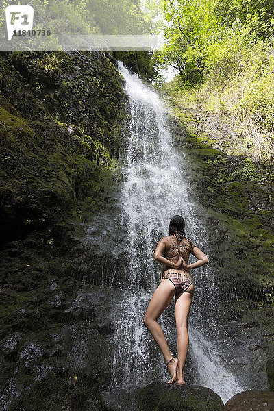 Kaukasische Frau steht auf einem Felsen in der Nähe eines Wasserfalls und macht Yoga