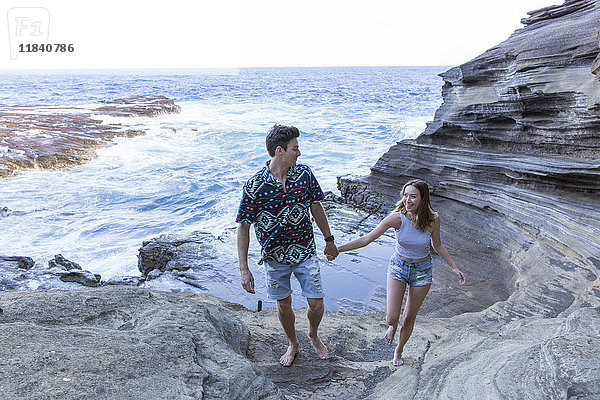 Lächelndes Paar  das am Strand auf Felsformationen spazieren geht