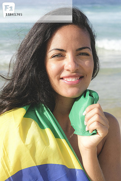 Junge brasilianische Frau  20 bis 29 Jahre alt  eingewickelt in die brasilianische Flagge an einem Strand in Rio de Janeiro  Brasilien  Südamerika
